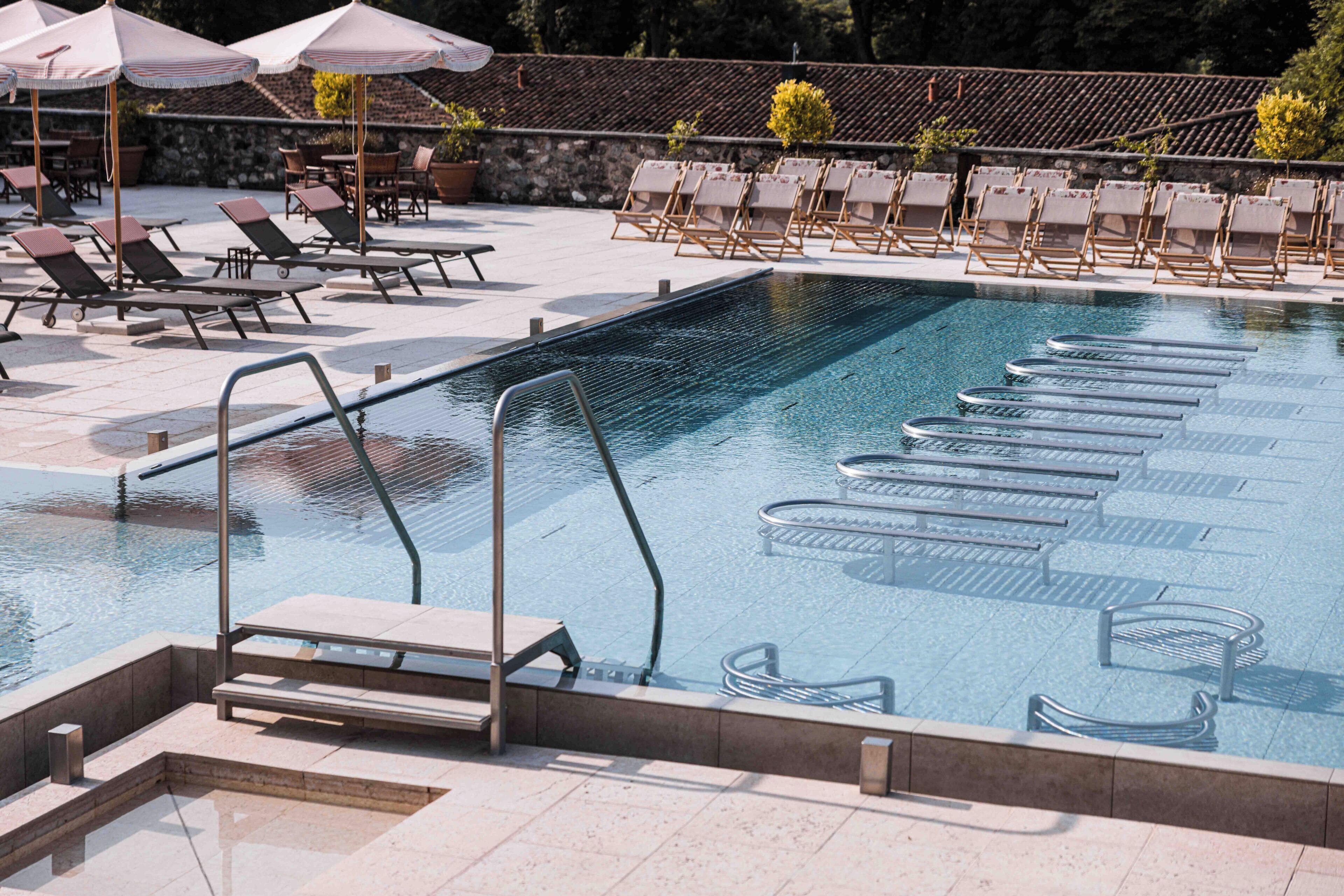 Una piscina con lettini e ombrelloni, circondata da un muro in pietra e piante in vaso.