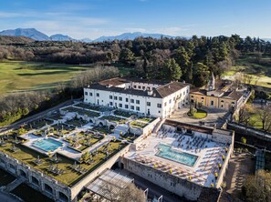 A large building with multiple pools and a well-maintained garden, surrounded by a mountainous landscape. - QC Grand Hotel Villa Arzaga Garda Spa & Golf (Calvagese della Riviera)