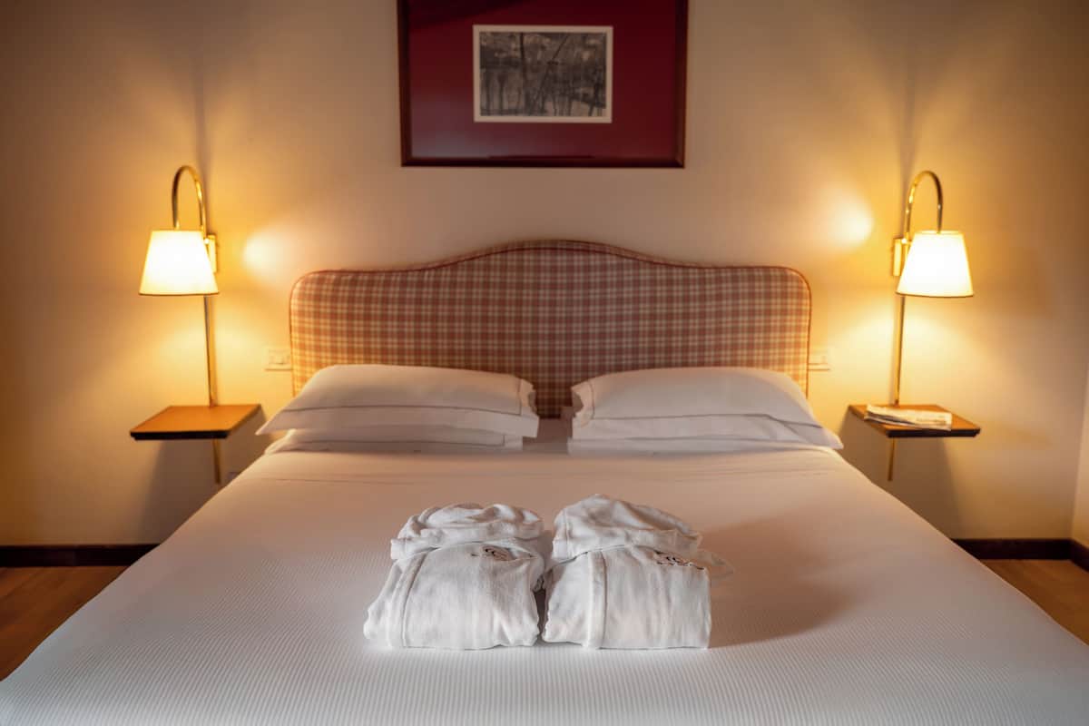 Un lit bien fait, avec du linge de lit blanc, deux lampes de chevet et une tête de lit à carreaux.