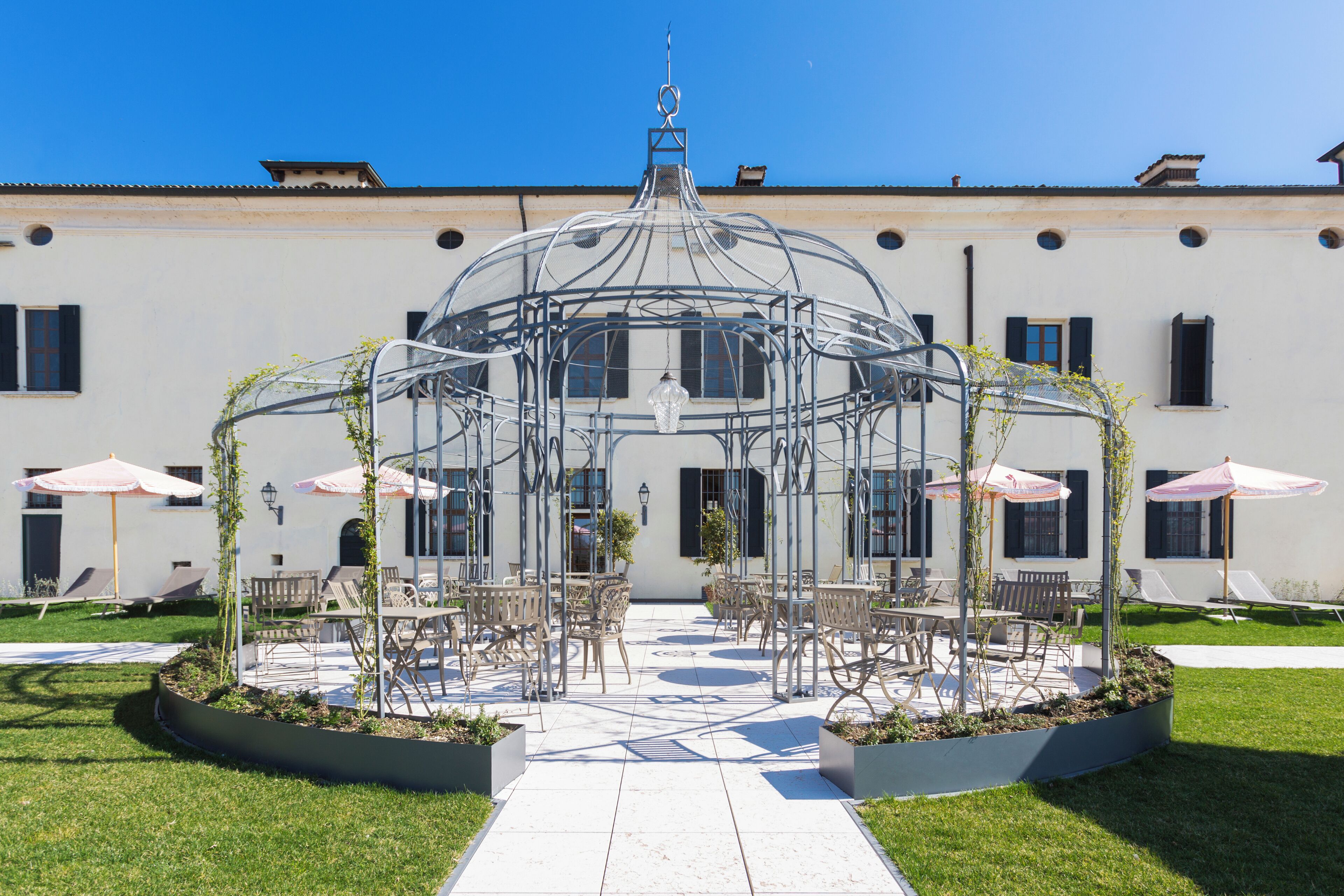 Un cortile con un gazebo in vetro, posti a sedere all'aperto e un vialetto che conduce all'edificio.