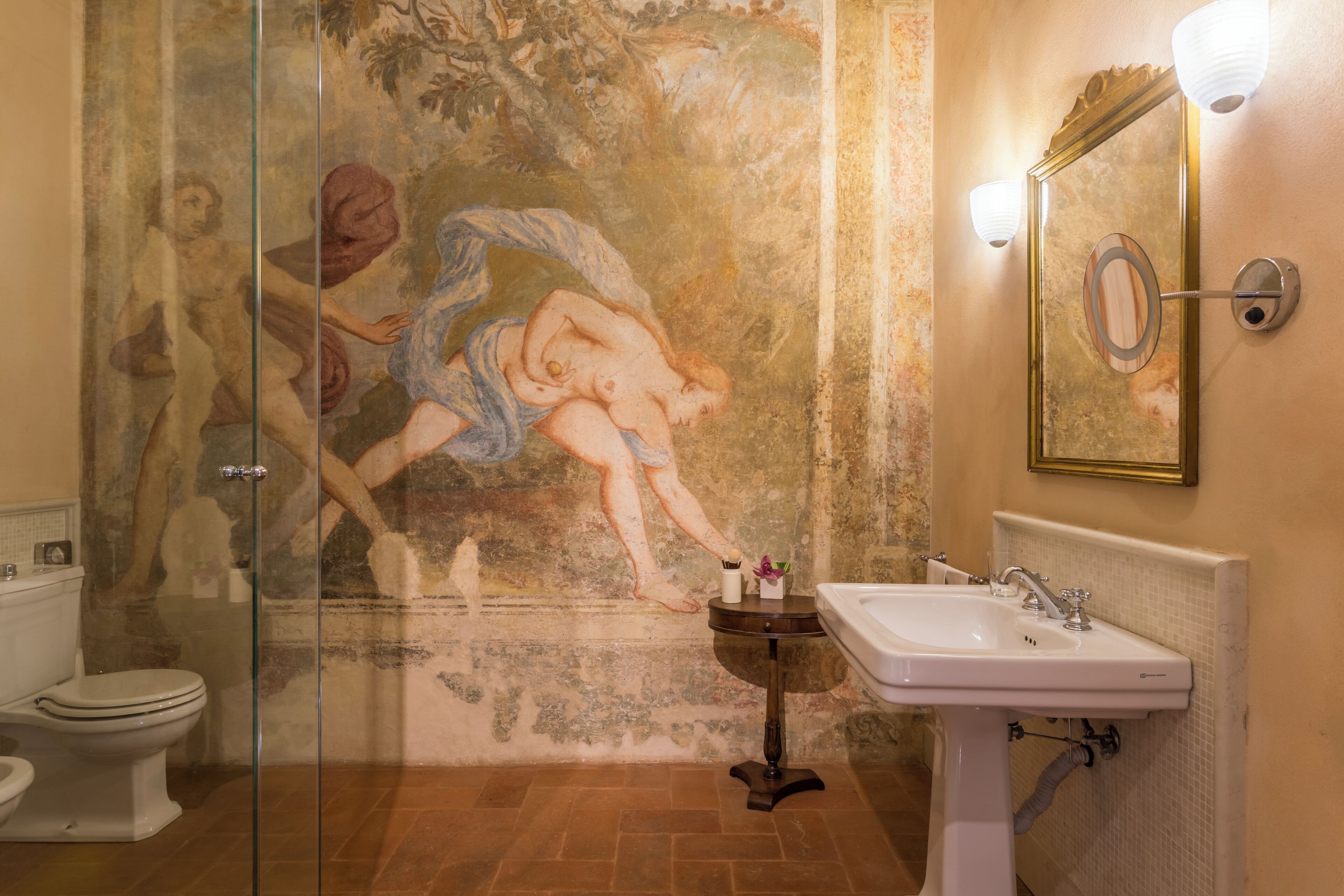 Une salle de bain avec un mur en marbre, une cabine de douche en verre, un lavabo blanc et un miroir avec un cadre doré.