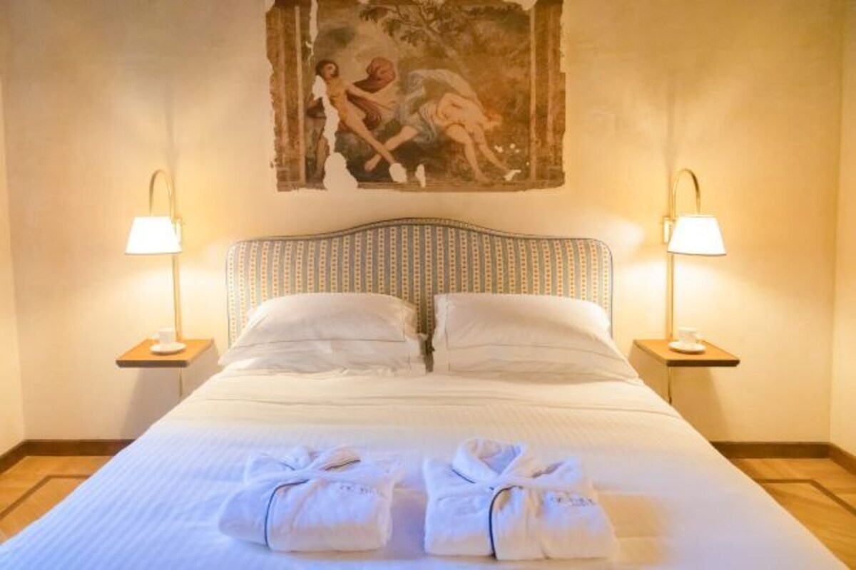 A neatly made bed with two pillows, two bedside lamps, and two towels on the bed.