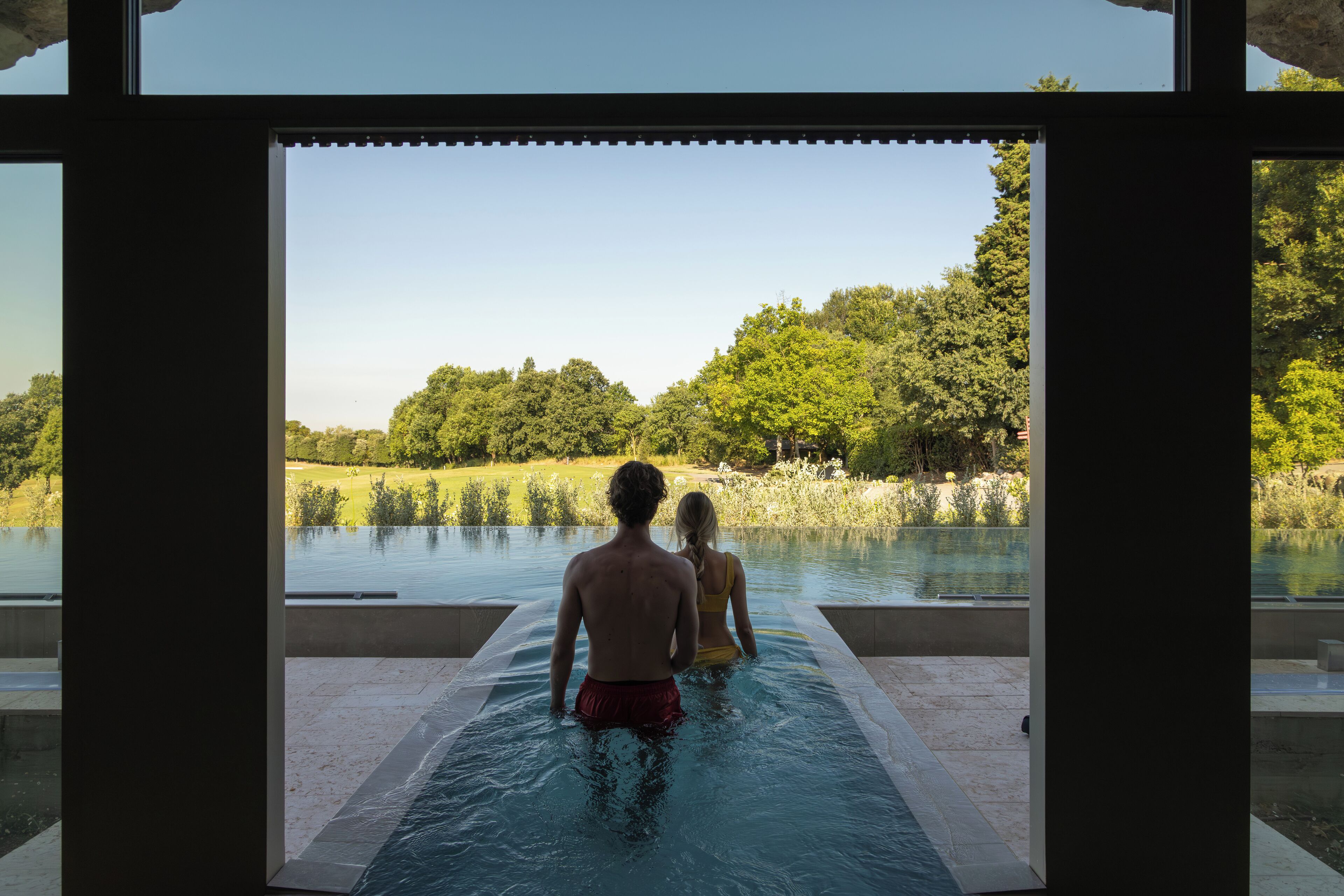Un hombre y una mujer en una piscina con vista a un lago y árboles.