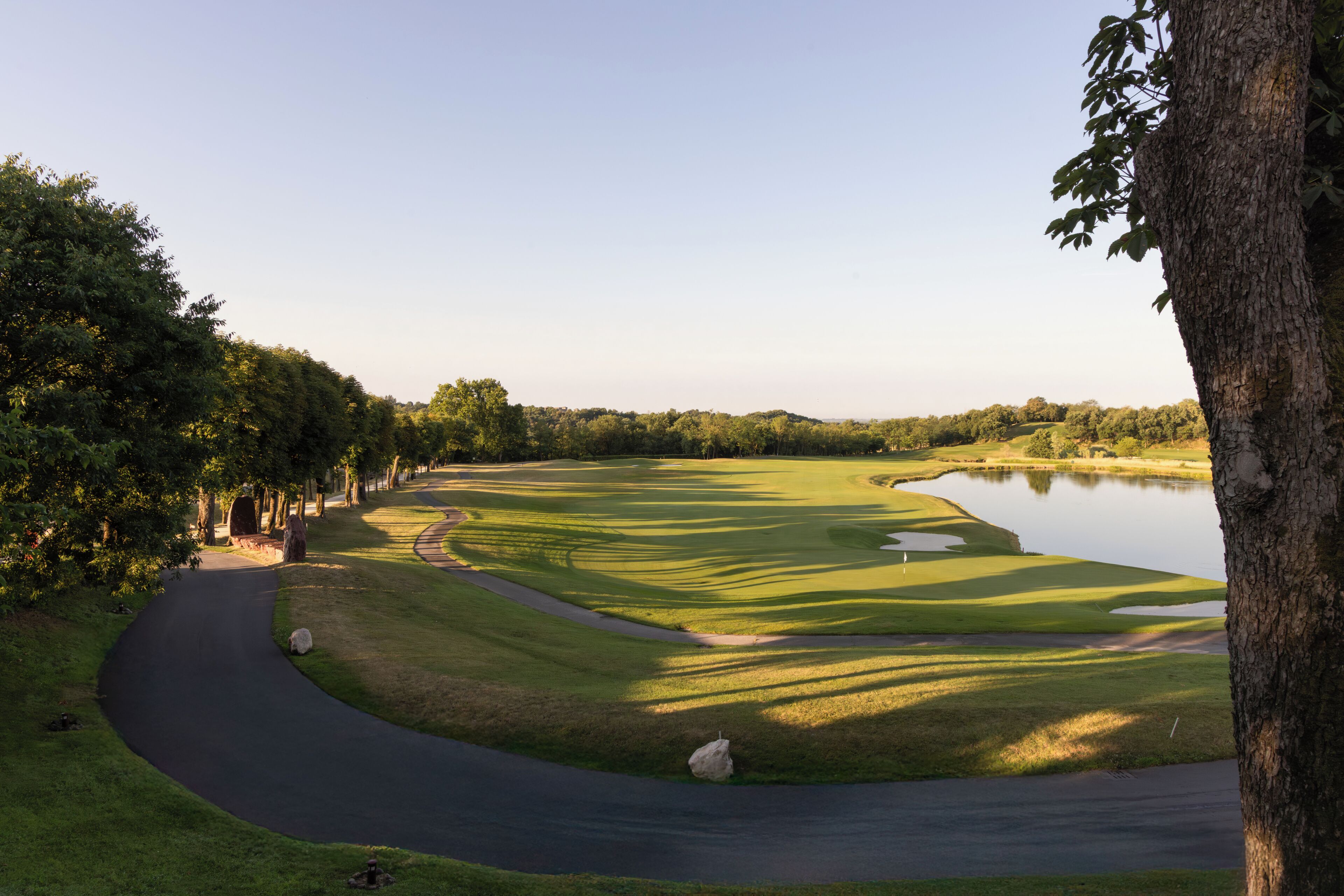 Un parcours de golf avec un plan d’eau, des arbres et un chemin sinueux.