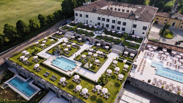 A large hotel with multiple swimming pools, a well-maintained garden, and a spacious outdoor area with numerous umbrellas and lounge chairs.