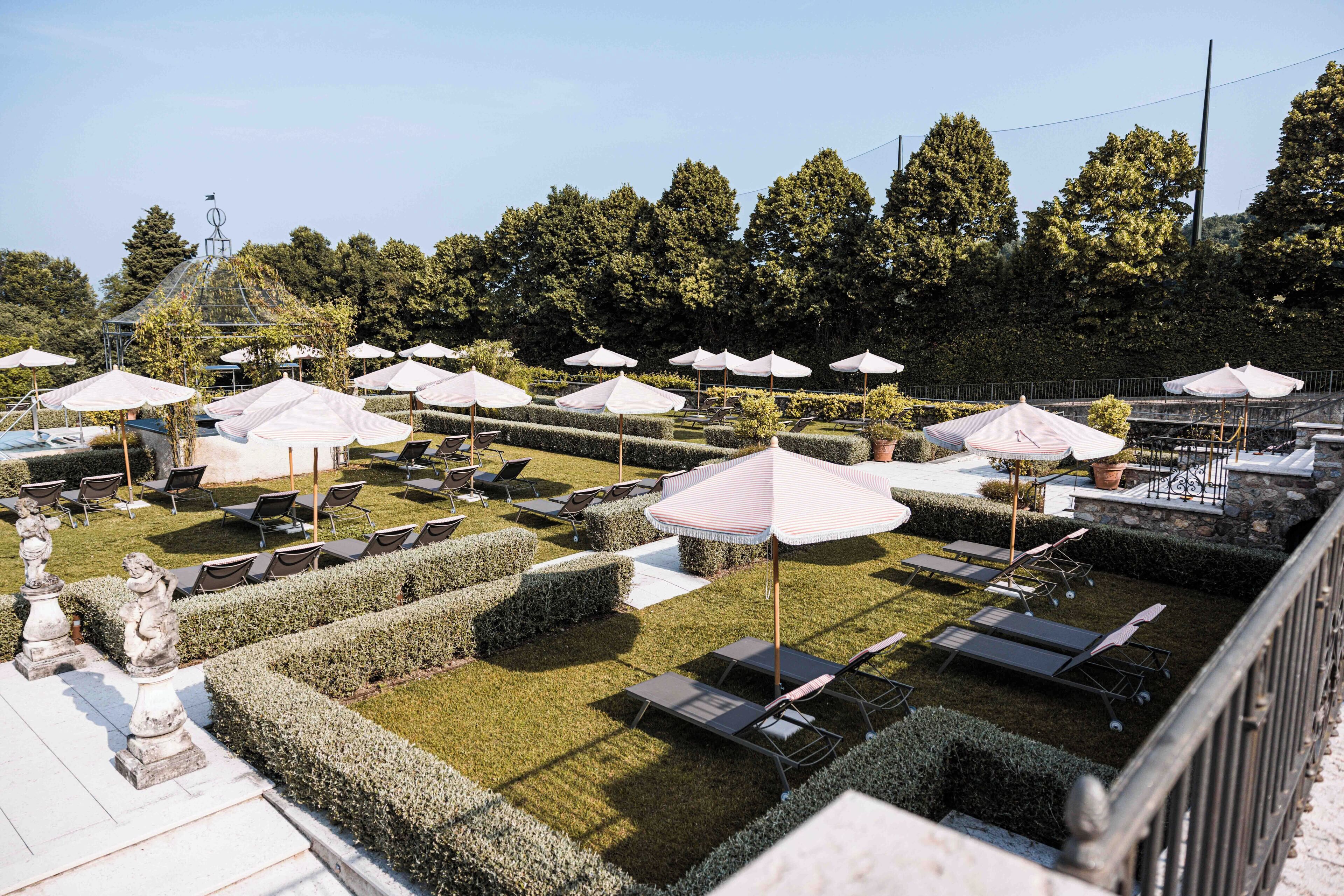 Un giardino curato con cura, dotato di confortevoli poltrone da esterno e ombrelloni, circondato da siepi e alberi.