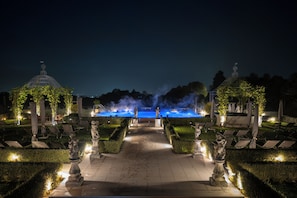 A nighttime outdoor area with a fountain, statues, and lounge chairs. - QC Grand Hotel Villa Arzaga Garda Spa & Golf (Calvagese della Riviera)