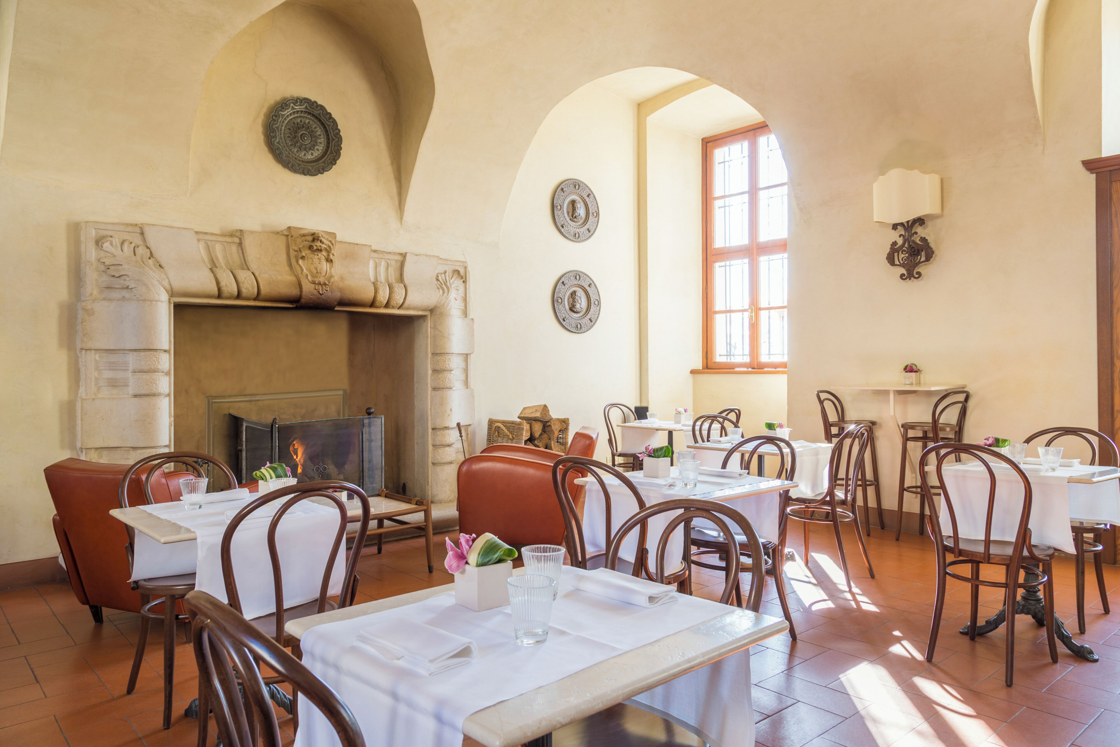 A dining area with tables, chairs, a fireplace, and decorative plates on the walls.