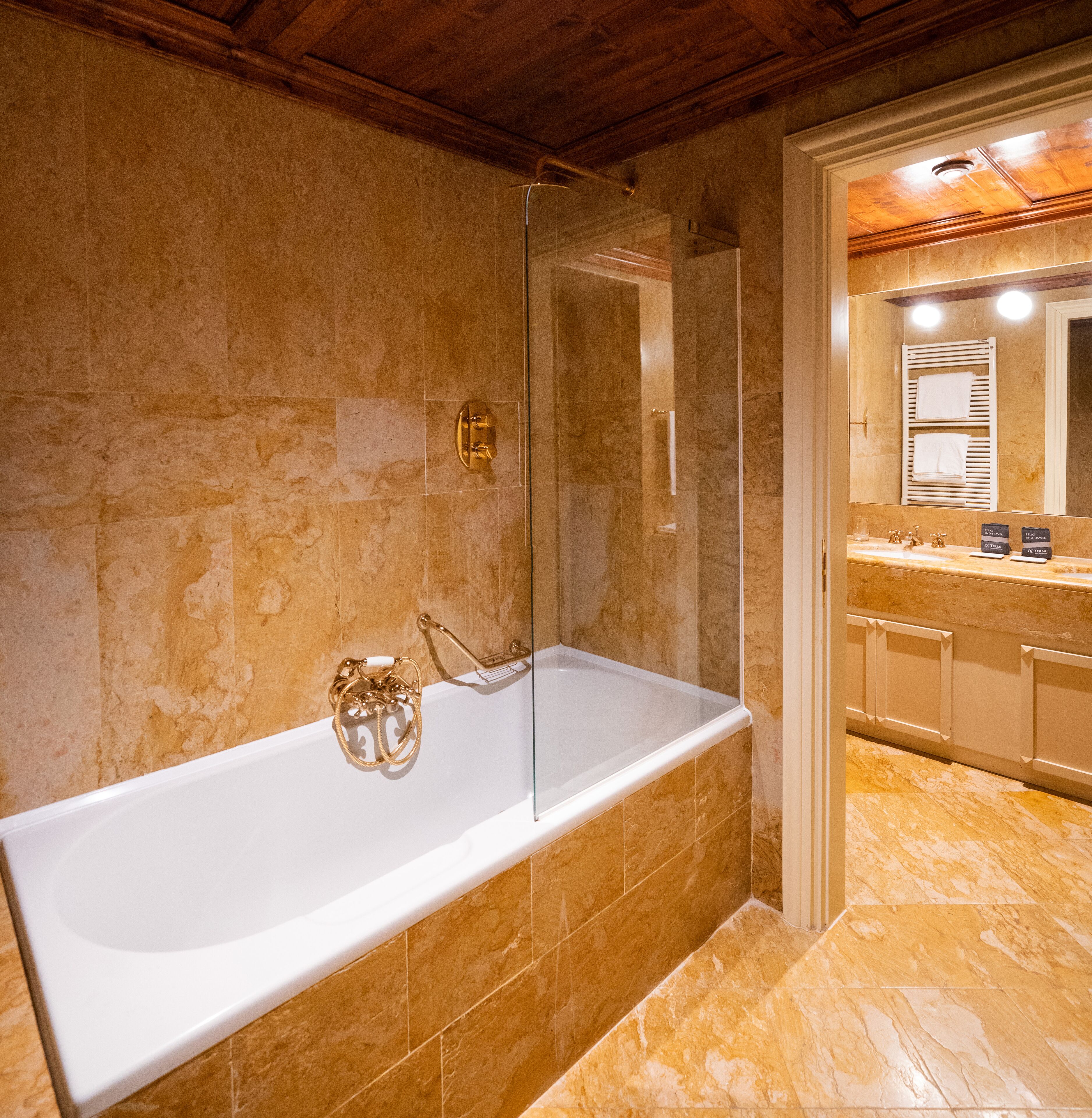 A modern bathroom with a glass-enclosed shower, a white bathtub, and a marble-tiled floor.