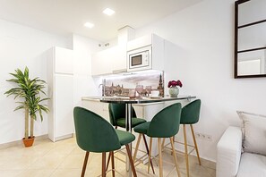 A modern kitchen with white cabinets, a built-in microwave, and a dining area with green chairs.
