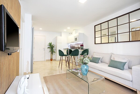A modern living room with a sofa, a glass coffee table, and a dining area with chairs.