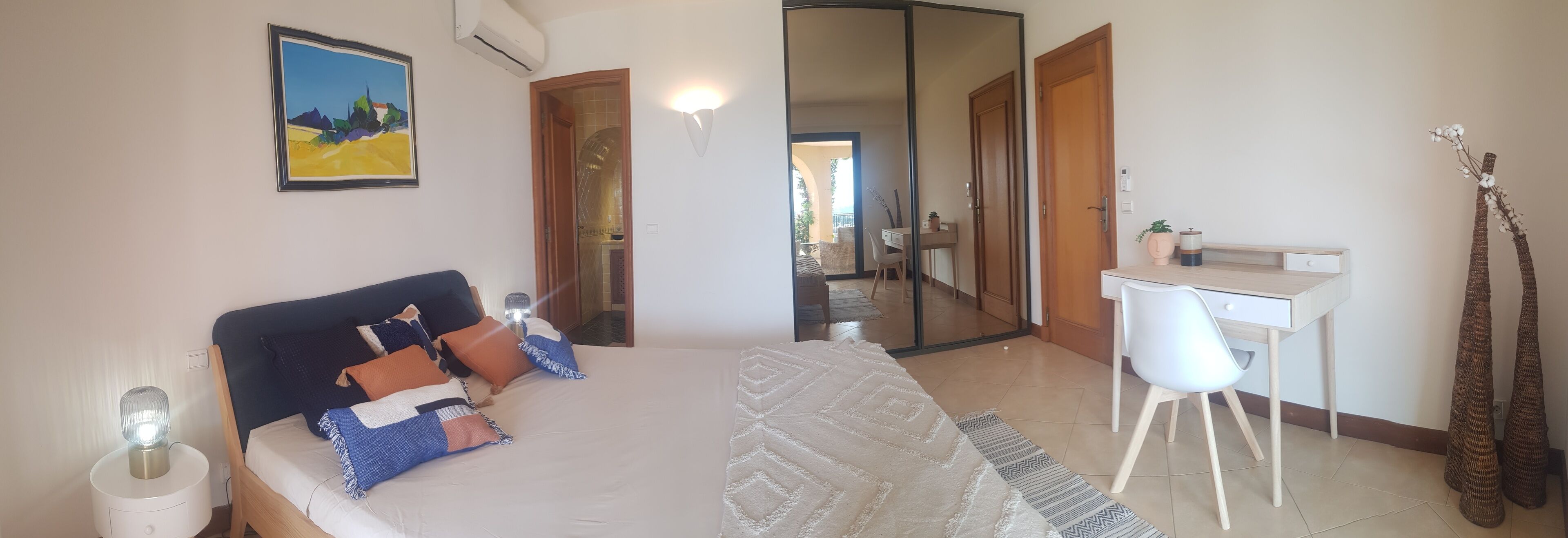 Een slaapkamer met een bed, nachtkastje, bureau, stoel en een grote spiegel.