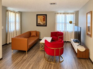 Una sala de estar moderna con un sofá, un sillón rojo, una mesa de centro y un televisor de pantalla plana.