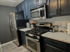 A kitchen with a refrigerator, microwave, stove, toaster, and a chalkboard with writing.