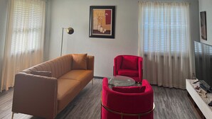 Una sala de estar moderna con un sofá marrón, una silla roja, una mesa de centro de vidrio y un televisor sobre un mueble.