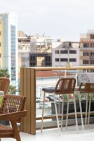 A balcony with wicker chairs and a table, overlooking a cityscape with modern buildings.