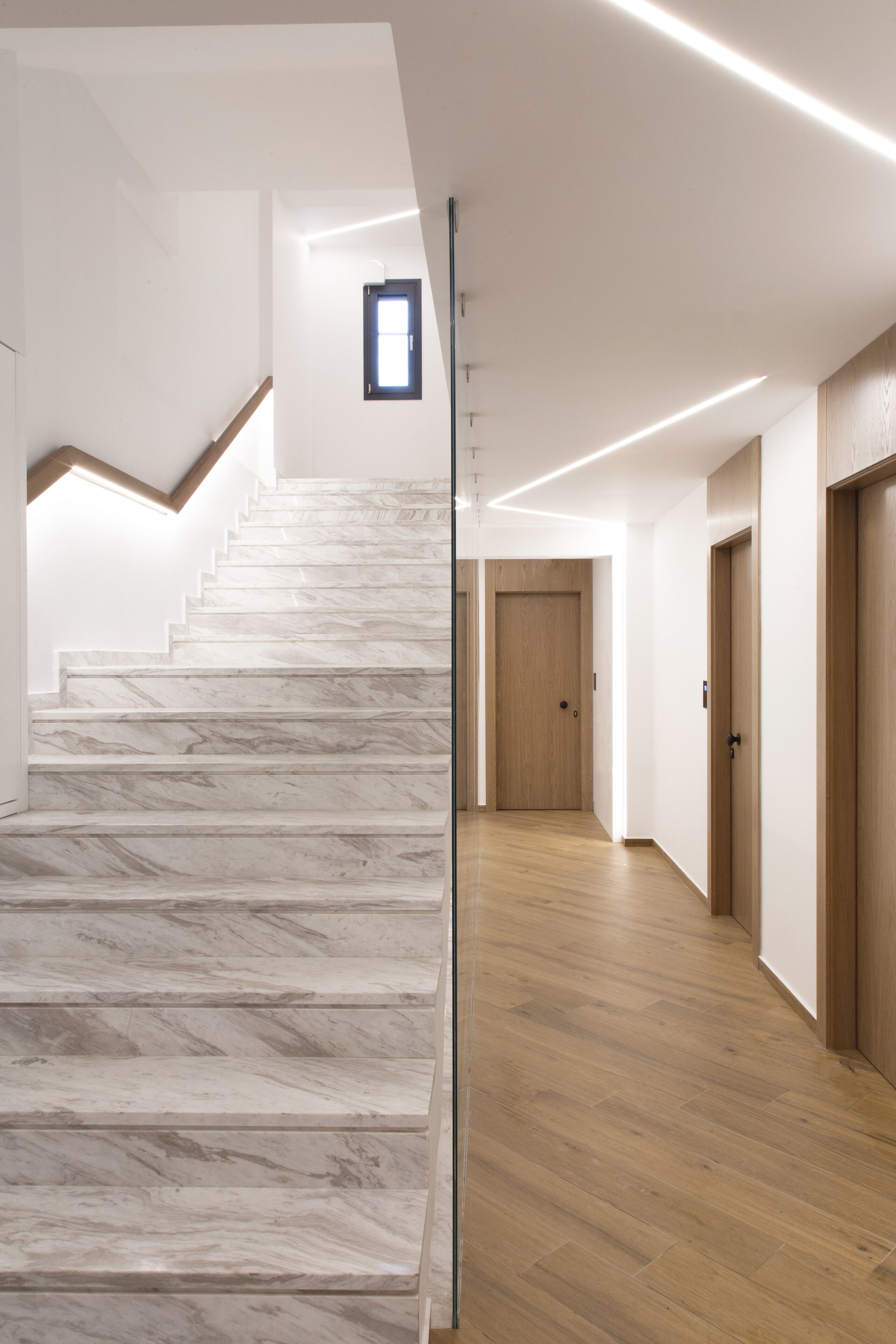 Una escalera de mármol conduce a una plataforma, con suelo de madera y una puerta al final del pasillo.