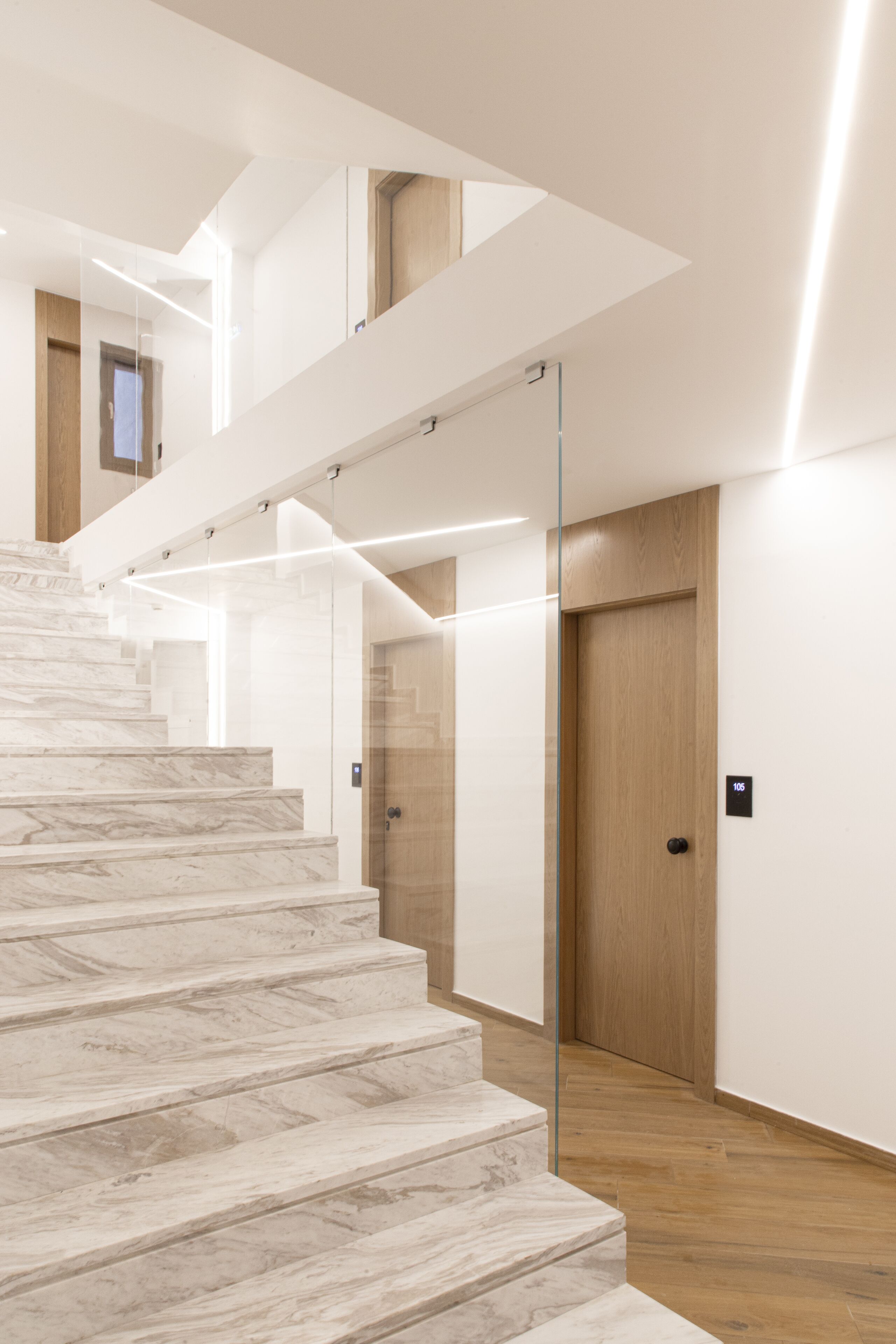 Un interior moderno con una escalera de mármol, suelo de madera y una partición de vidrio.