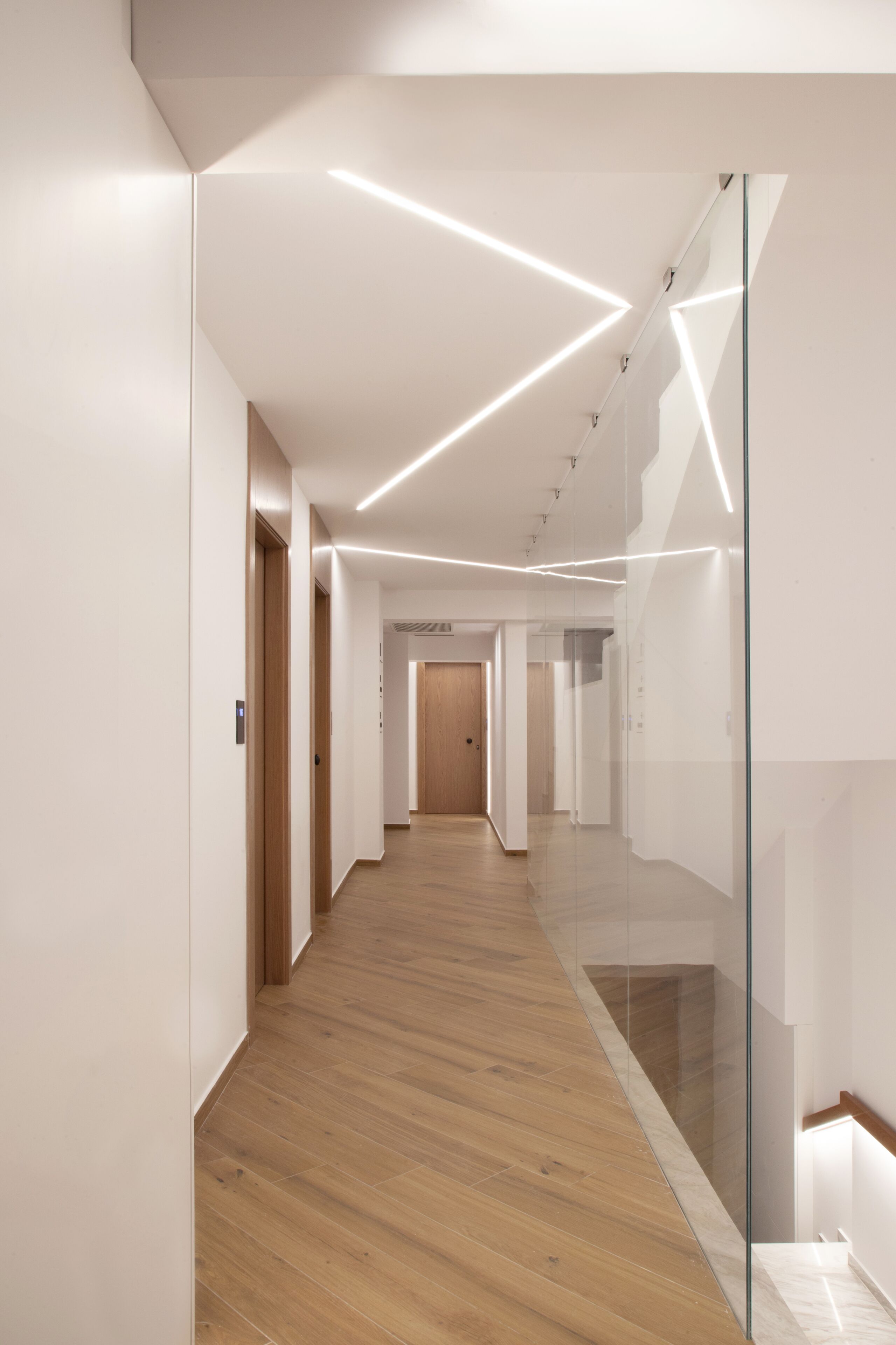 Un passadís modern amb terres de fusta, parets de vidre i il·luminació empotrada.