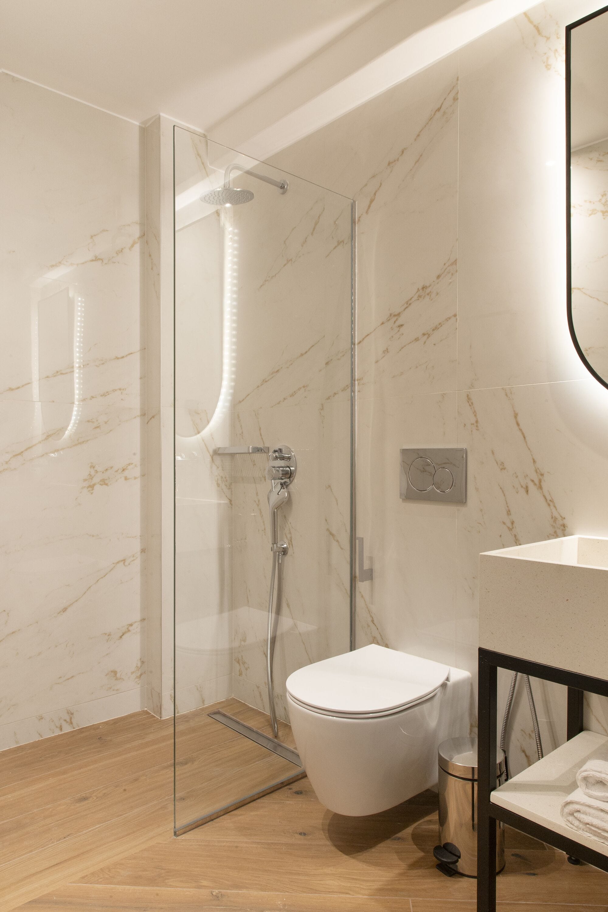 A modern bathroom with a glass-enclosed shower, a white toilet, and a wooden floor.