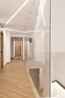 Un pasillo moderno con suelo de madera, divisiones de vidrio e iluminación empotrada.