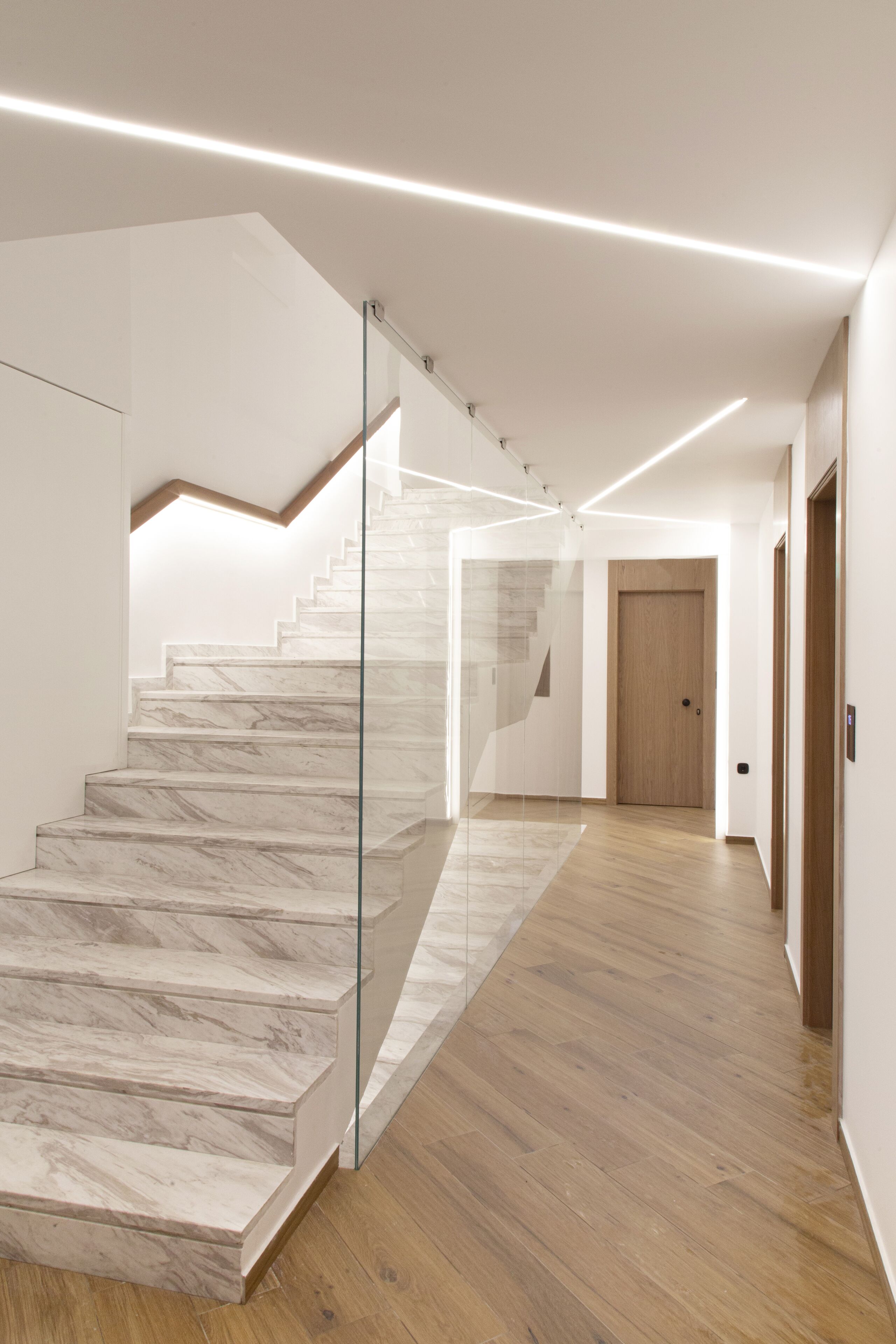Un interior moderno con una escalera de mármol, suelo de madera y un separador de vidrio.