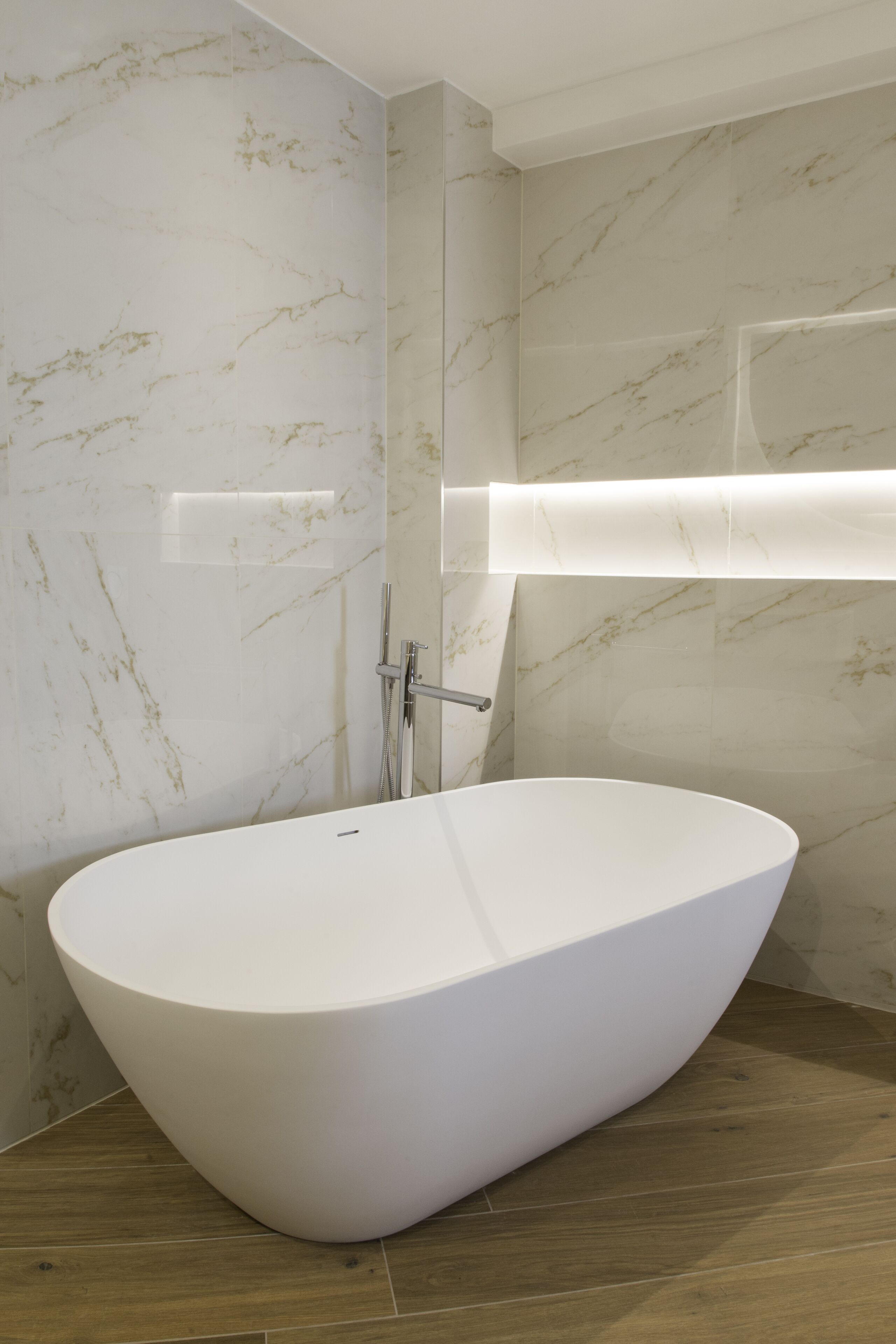 A modern bathroom with a freestanding bathtub, marble walls, and a wooden floor.