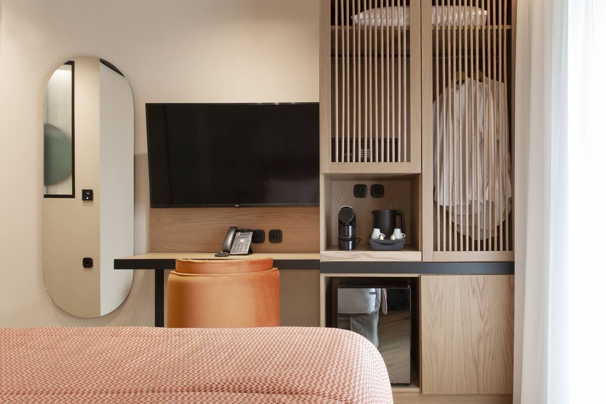 A modern hotel room with a large bed, a desk with a telephone, a television, and a wooden cabinet with a coffee maker.