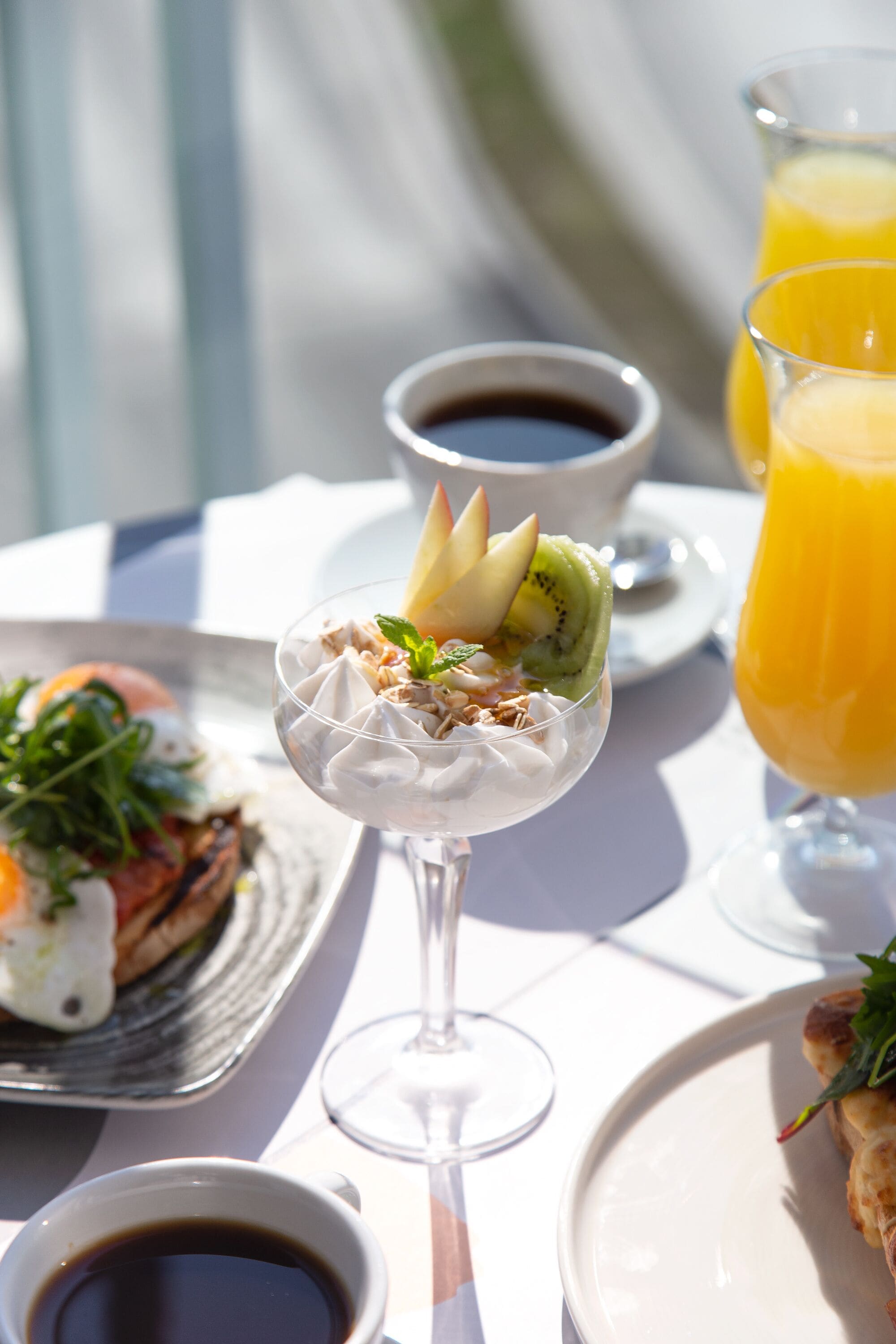 A table with a dessert in a glass, a cup of coffee, and a glass of orange juice.