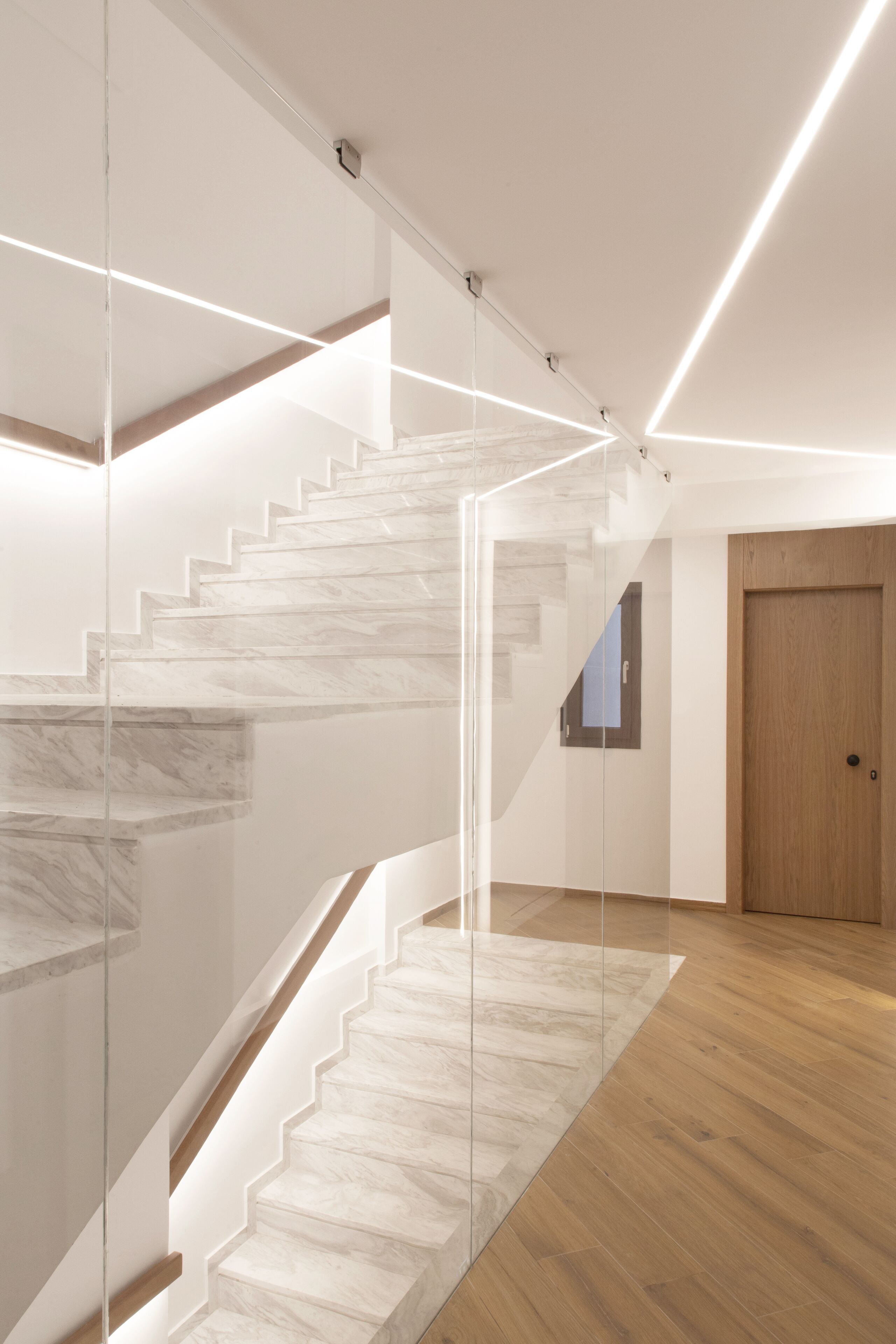 Una escalera moderna con barandillas de cristal y escalones de madera.