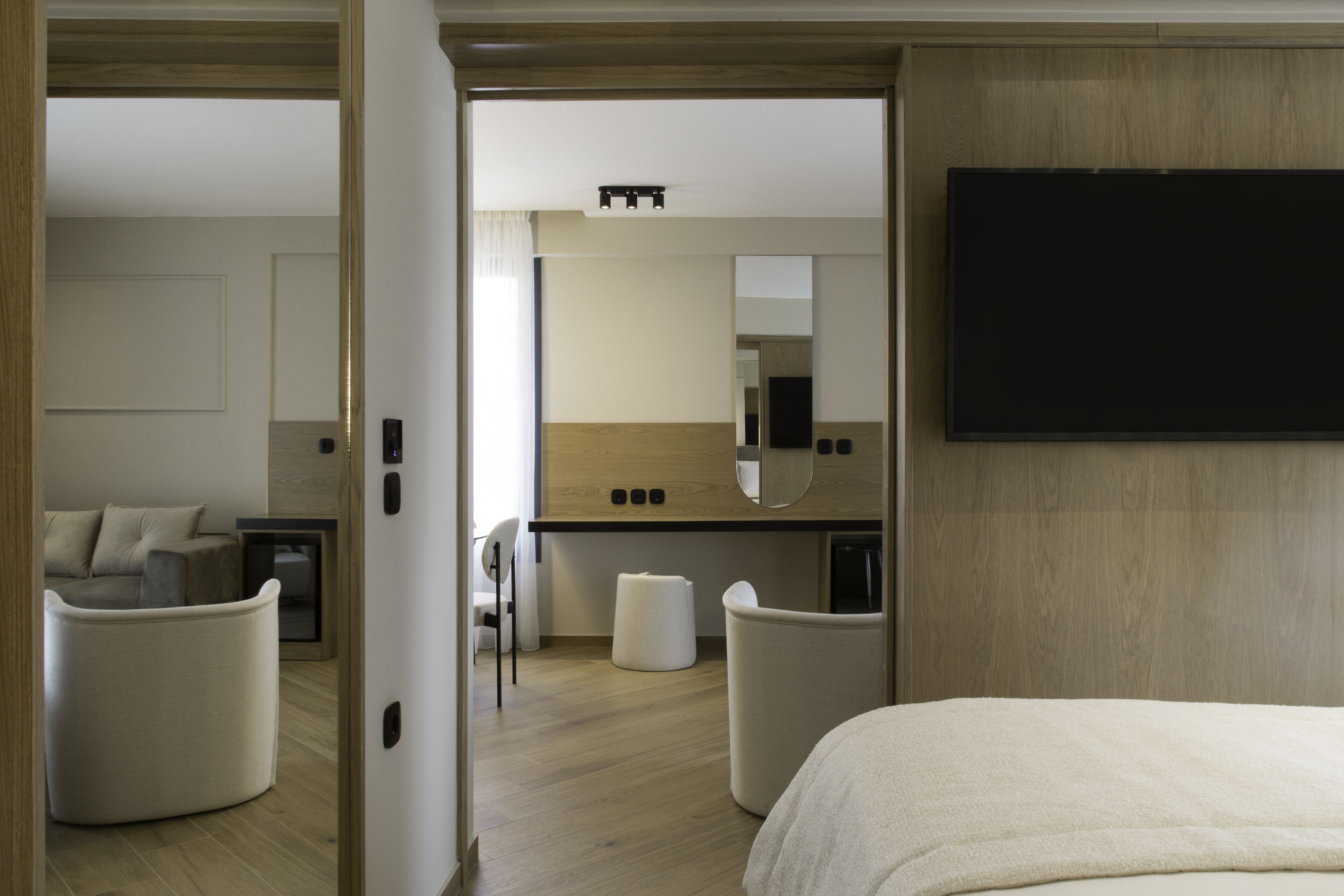 A modern hotel room with a bed, a TV, a kitchenette, and a seating area with chairs.