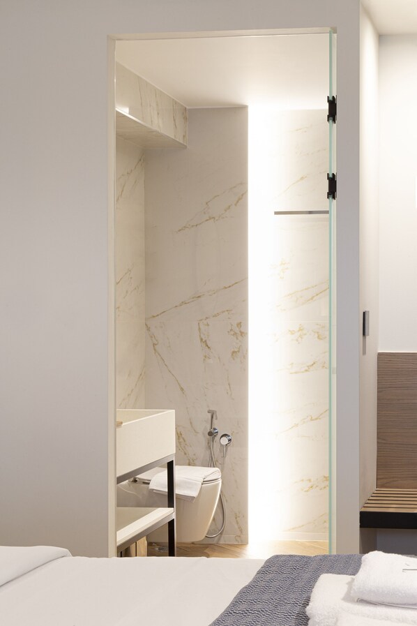 A modern bathroom with a glass shower enclosure, a white toilet, and a wooden vanity. - 1910 Lifestyle Hotel (Volos)