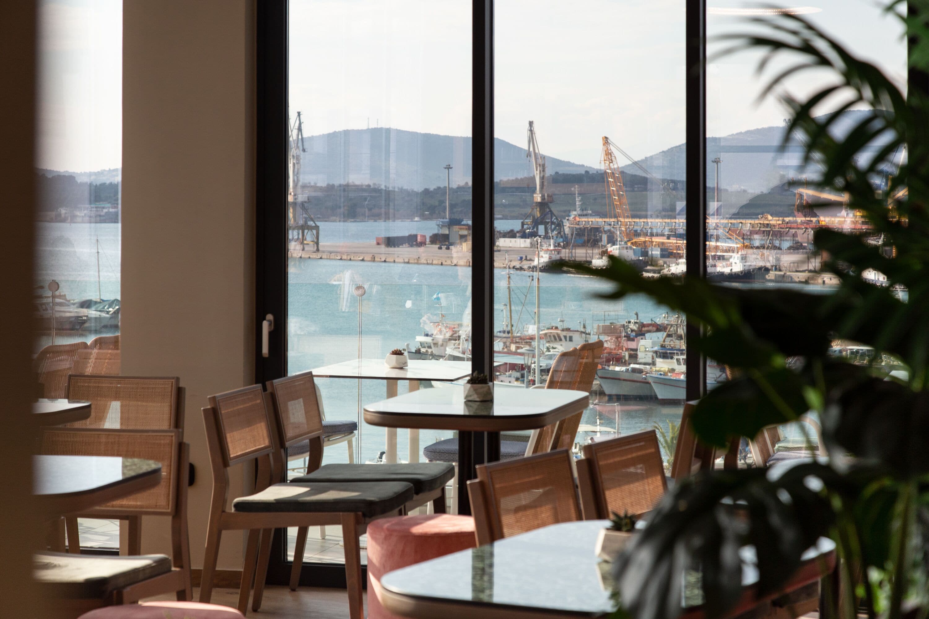 A restaurant with large windows overlooking a harbor, featuring several tables and chairs.