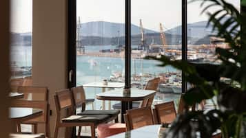 A restaurant with large windows overlooking a harbor, featuring several tables and chairs.