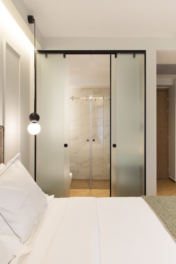 Un dormitorio moderno con cama, lámpara de noche y puerta corredera que da a un baño.