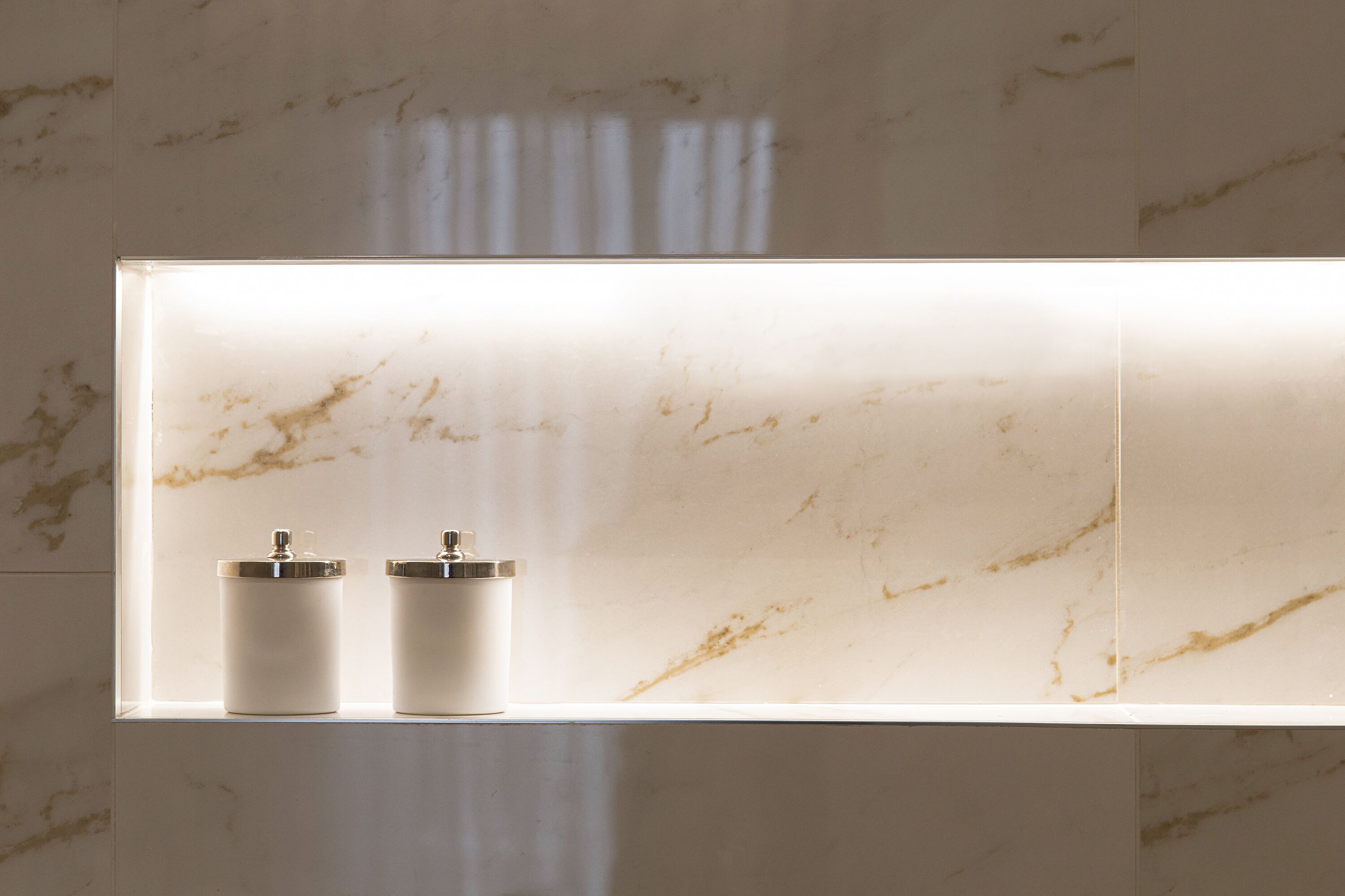 A bathroom with a marble wall and two white dispensers on a shelf.