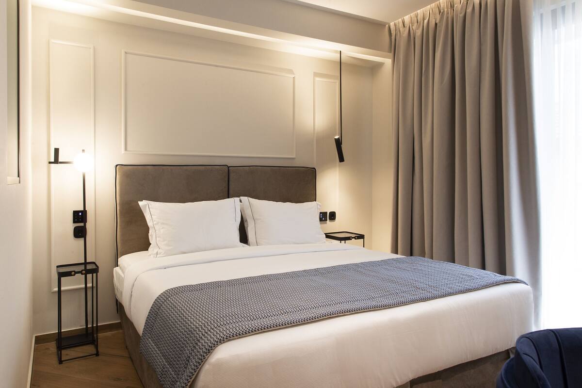 A hotel room with a bed, bedside tables, a lamp, and a curtain.
