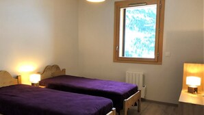 A small, simple room with two wooden beds, a window with a view of trees, and a radiator.