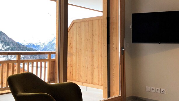 A room with a wooden balcony, a green chair, and a TV mounted on the wall.