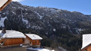 A wooden cabin with a snow-covered roof, surrounded by a forested mountain landscape.