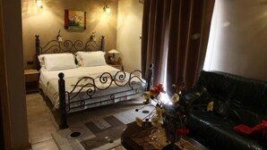 A bedroom with a bed, a nightstand, a lamp, a vase with flowers, a black leather sofa, and a painting on the wall. - Hotel Tutto (Hotel Tutto)