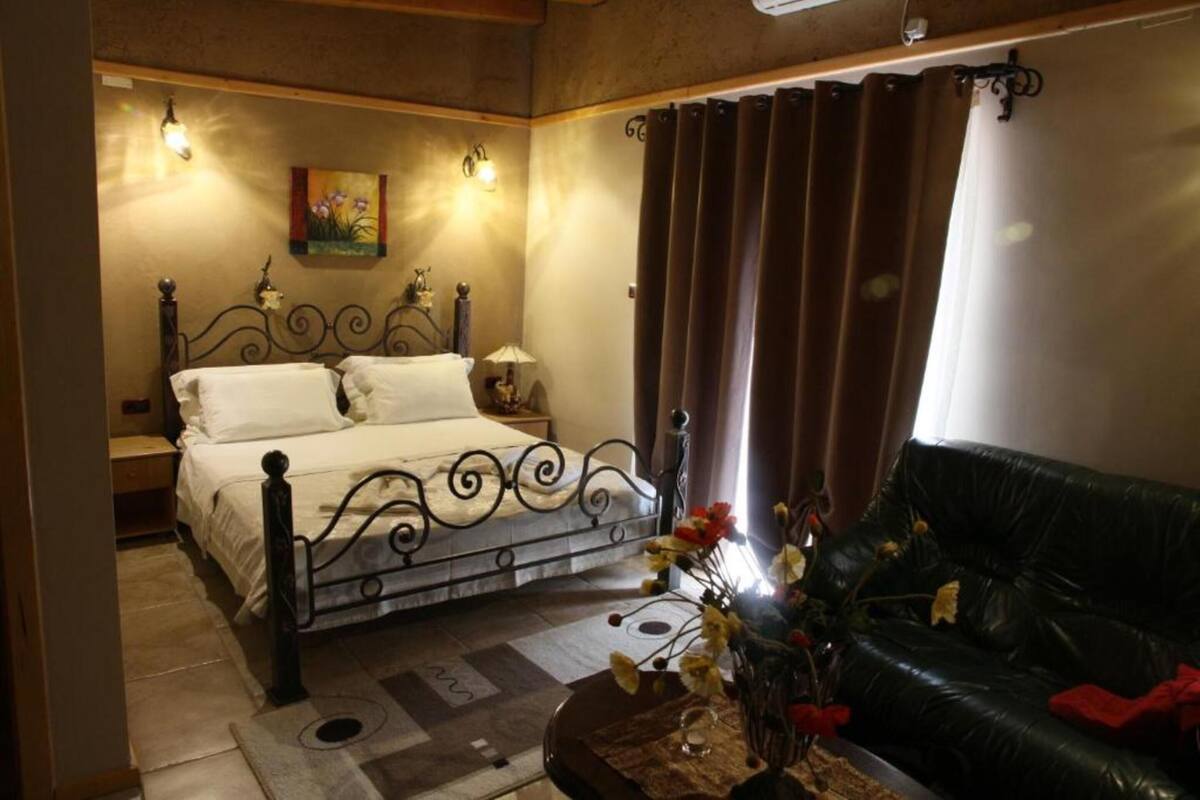 Un dormitorio con una cama, una mesita de noche, una lámpara, un florero con flores, un sofá de cuero negro y un cuadro en la pared.