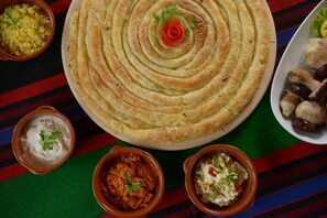 A large, round pastry with concentric layers, surrounded by small bowls of dips and side dishes on a colorful striped tablecloth.