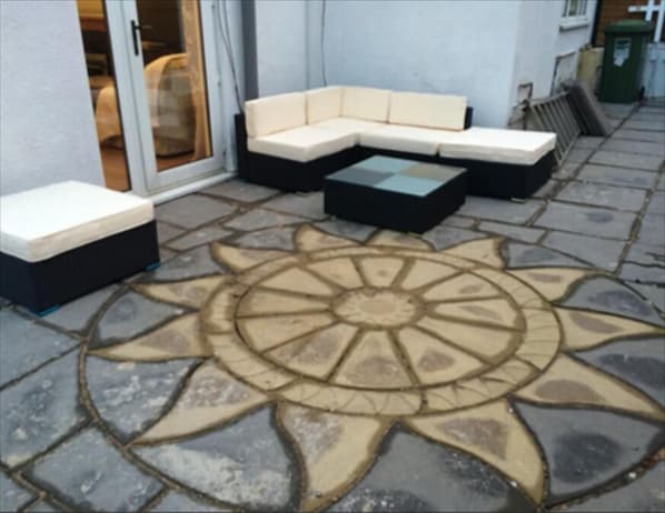 A patio with a sectional sofa and a small table, a patterned stone floor, and a sliding glass door leading to an interior space.