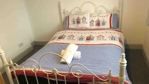 Un lit simple avec un cadre en métal, une couvre-lit à carreaux et des coussins assortis.