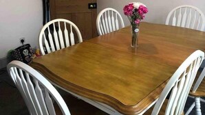 Une table à manger entourée de six chaises blanches, une porte en bois et un vase rempli de fleurs posé sur la table.