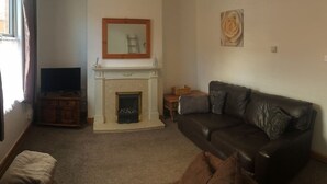 A living room with a fireplace, a leather sofa, a television, and a painting on the wall. - Kettering Town Corporate - Ford Street (Kettering)
