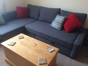 A sectional sofa with red and grey pillows, a wooden coffee table with books, and a carpeted floor.