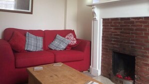 A red sofa with patterned cushions, a wooden coffee table, a fireplace, and a framed picture on the wall.