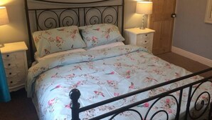 A bed with floral bedding, two bedside tables with lamps, a wooden door, and a metal bed frame.
